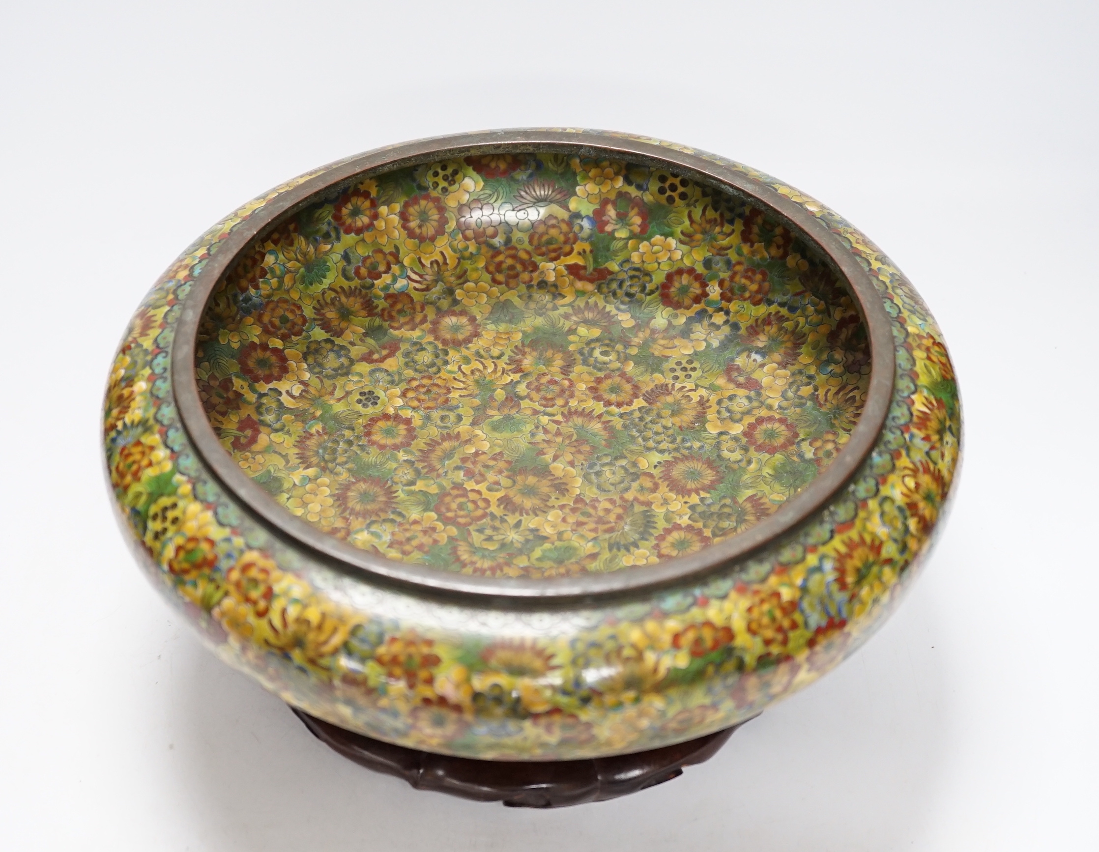 A Chinese circular cloisonné enamel bowl decorated with multi-coloured flowerheads on wooden stand, 30cm diameter